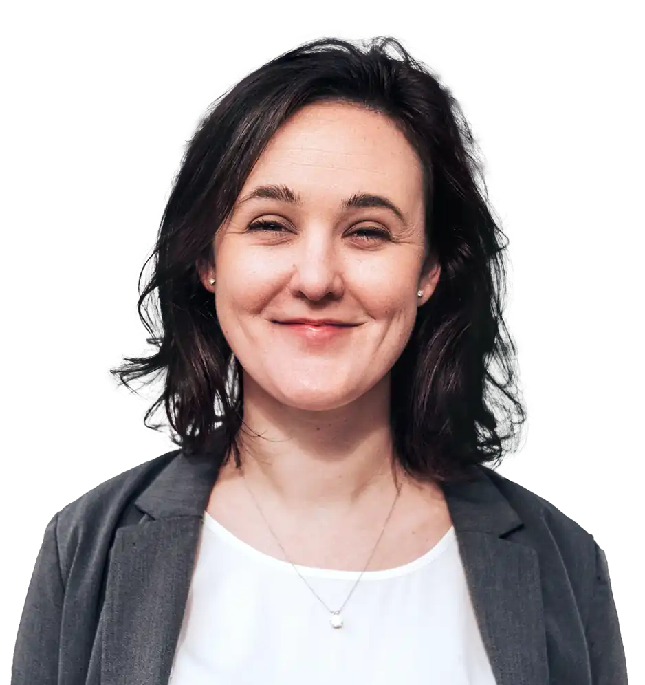 A woman smiling brightly, her brown eyes nearly closing. She has shoulder-length dark hair, curling slightly towards the ends. She is wearing a dark gray blazer on a white shirt, and a silver necklace to accompany her stud earrings.